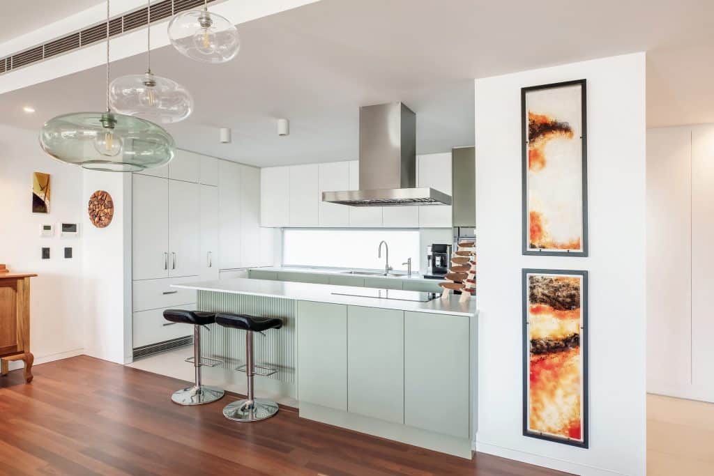 Open-concept kitchen with a pale green island, white cabinets, a stainless steel range hood, and two black-bar stools.