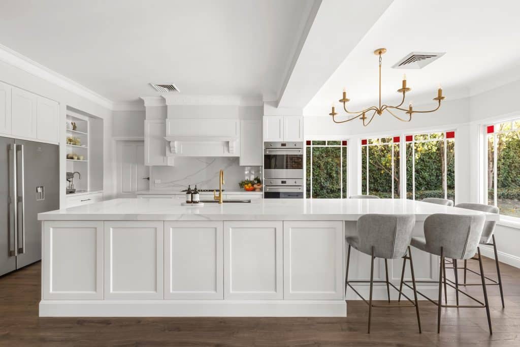 Bright white kitchen with a large marble island, gold faucet, and gold chandelier lighting the space