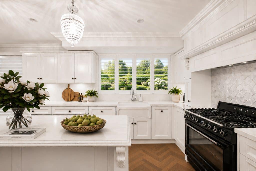 Bright white kitchen with marble countertops, central island, and a bowl of pears on the island.