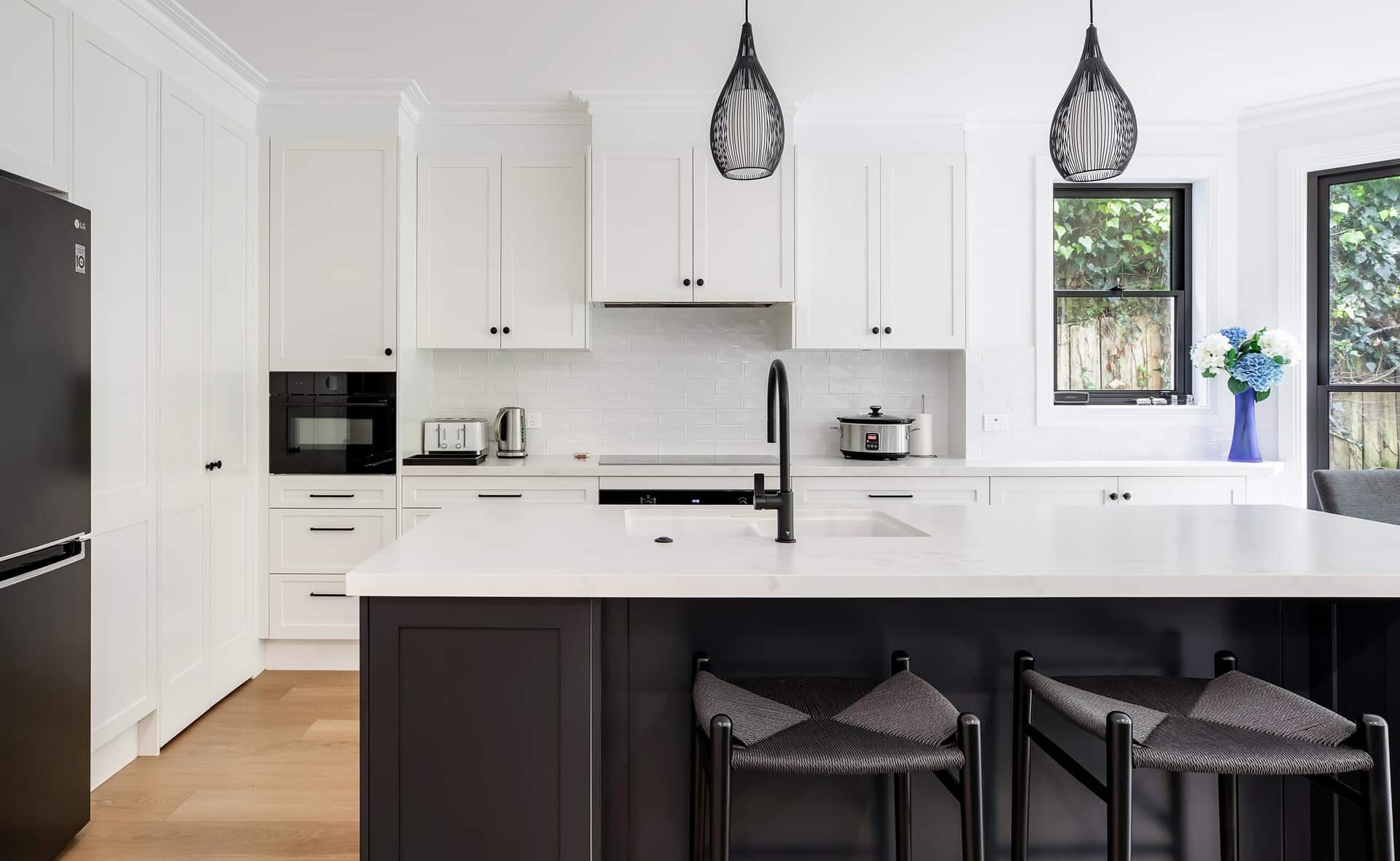Bright white kitchen with a central island, black faucet, and pendant lights above the island.