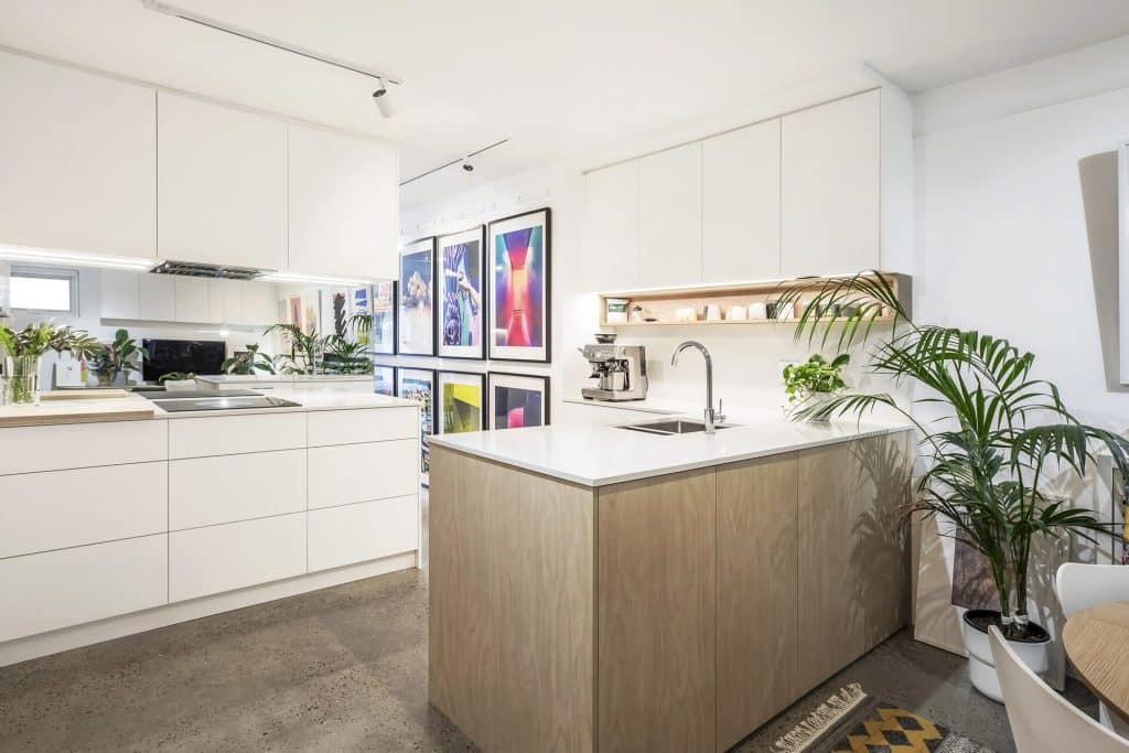 Bright contemporary kitchen with white cabinets, a wooden island, and framed art along the wall. (Informative)