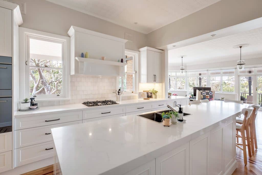 White kitchen with a large island, gas stove, subway tile backsplash, and tall windows opening to a bright living area.